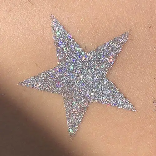 Tatouage pailleté en forme d’étoile réalisé avec un pochoir adhésif, de la colle cosmétique et des paillettes brillantes.