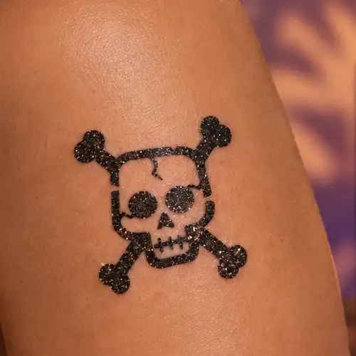 Tatouage pailleté tête de mort avec crâne et os croisés réalisé avec un pochoir sur la peau, motif pirate pour Halloween.