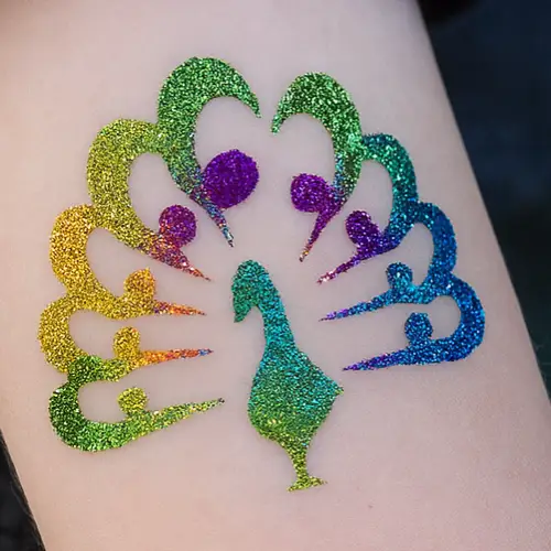 Tatouage temporaire paon réalisé avec un pochoir, de la colle pour la peau et des paillettes multicolores.