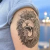 Tatouage temporaire tête de lion avec plumes, en noir et gris réaliste.