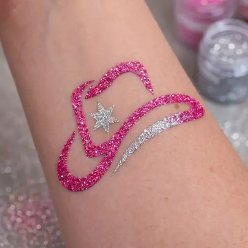 Tatouage pailleté en forme de chapeau de cow-boy, réalisé avec des paillettes roses et argentées appliquées avec un pochoir et de la colle cosmétique.