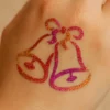 Tatouage temporaire pailleté en forme de deux cloches, réalisé à l’aide d’un pochoir adhésif.
