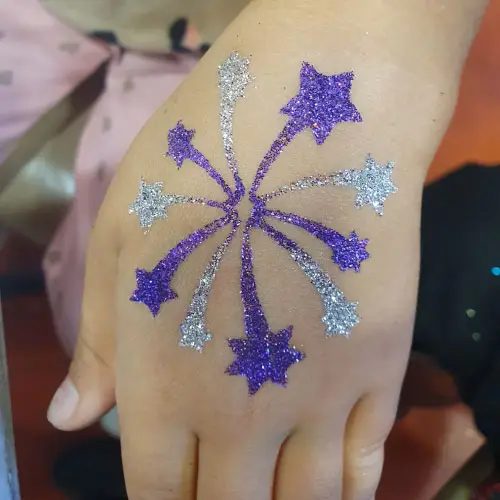 Tatouage éphémère feux d’artifice, réalisé avec un pochoir autocollant, colle cosmétique et paillettes cosmétiques.