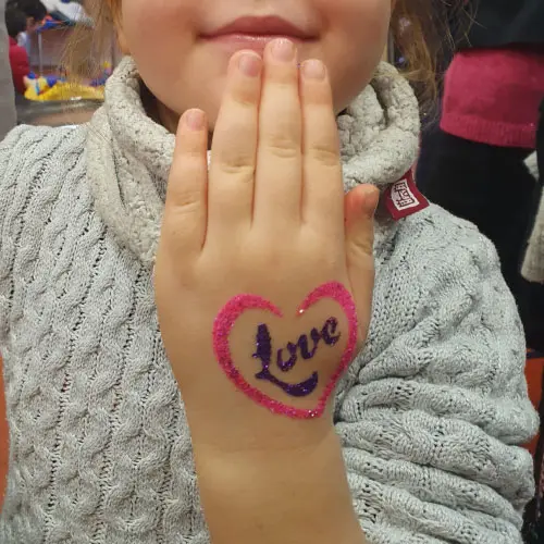 Pochoir tatouage Love Heart en forme de cœur avec le mot “love” à l’intérieur, utilisé pour créer un tatouage éphémère avec des paillettes et de la colle cosmétique.