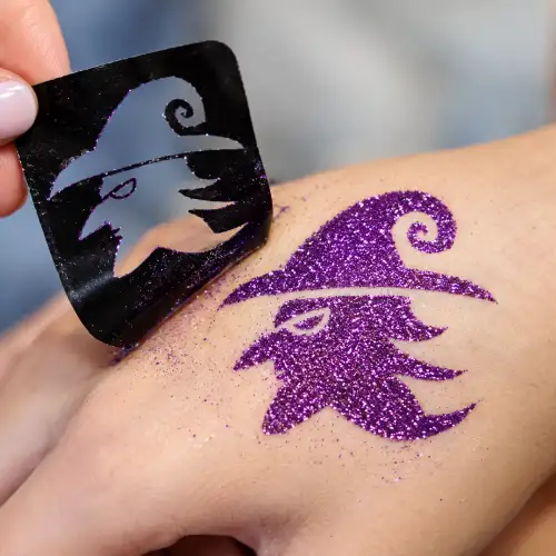Tatouage pailleté sorcière Halloween réalisé avec un pochoir, de la colle cosmétique et des paillettes sur la peau.