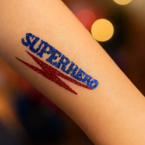 Tatouage pailleté représentant le mot “SUPERHERO” en paillettes bleu roy avec un éclair rouge brillant en dessous