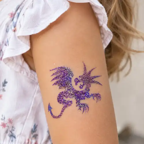 Tatouage paillette dragon réalisé sur le bras d’un enfant, motif dragon brillant avec des paillettes cosmétiques.