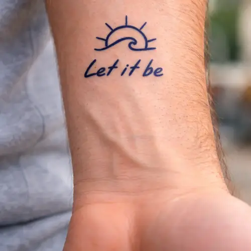 Tatouage semi-permanent au jagua, représentant une vague stylisée avec un petit soleil et la phrase « Let it be ». Le tatouage est de couleur bleu nuit profond, minimaliste, discret et réaliste, conçu pour durer 8 à 15 jours.