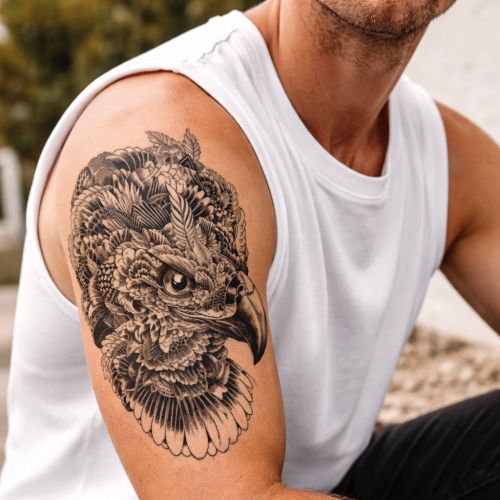 Tatouage temporaire d’une tête d’aigle réaliste en noir et gris, composé de plumes finement dessinées.